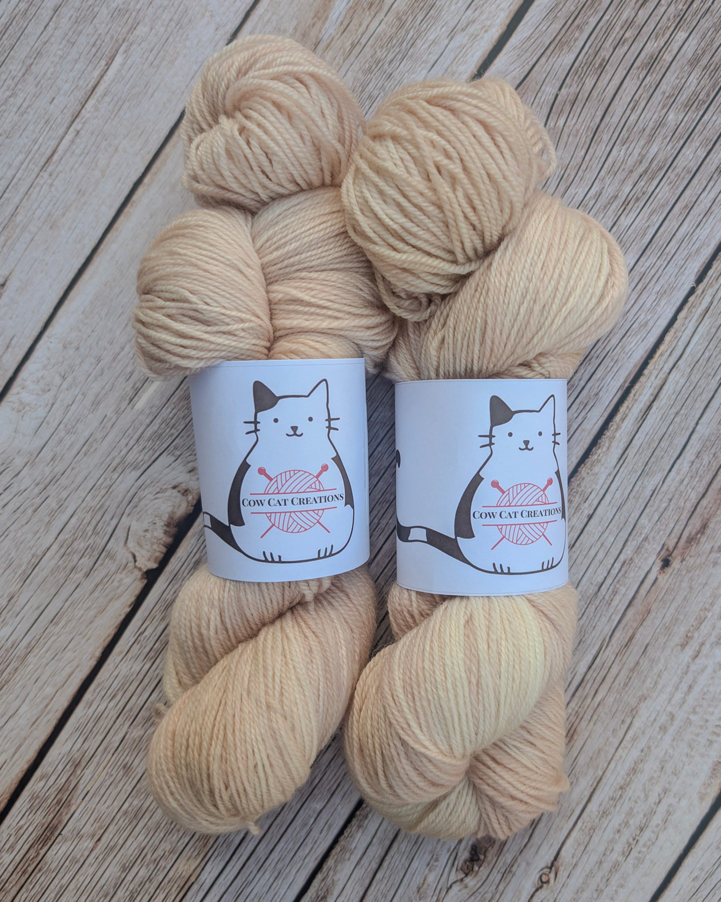 Two skeins of beige yarn with labels on a wooden surface