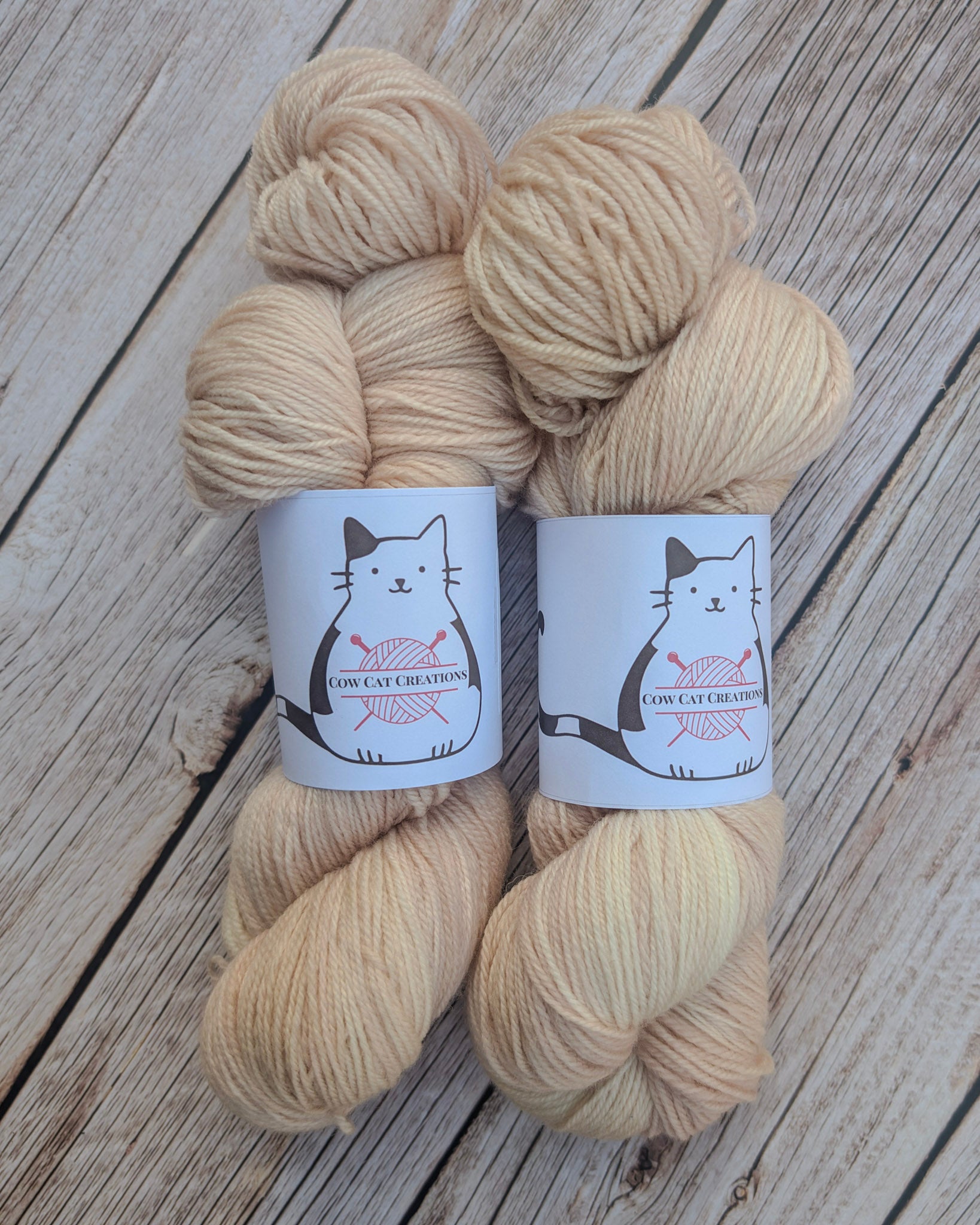 Two skeins of beige yarn with labels on a wooden surface
